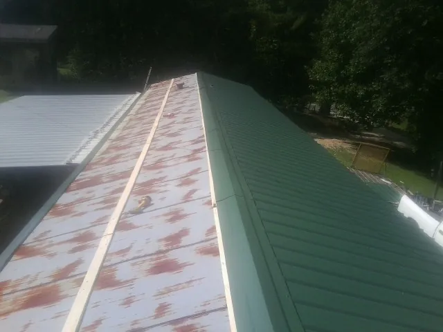 Old rusted panels beside newly installed green metal roofing — Wind Damage Roof Repair by Roofing Brothers in Melrose